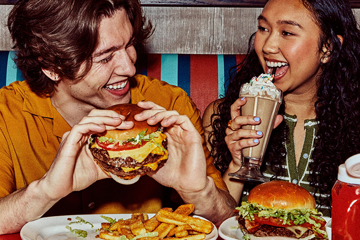 Man eating a burger and woman eating a shake
